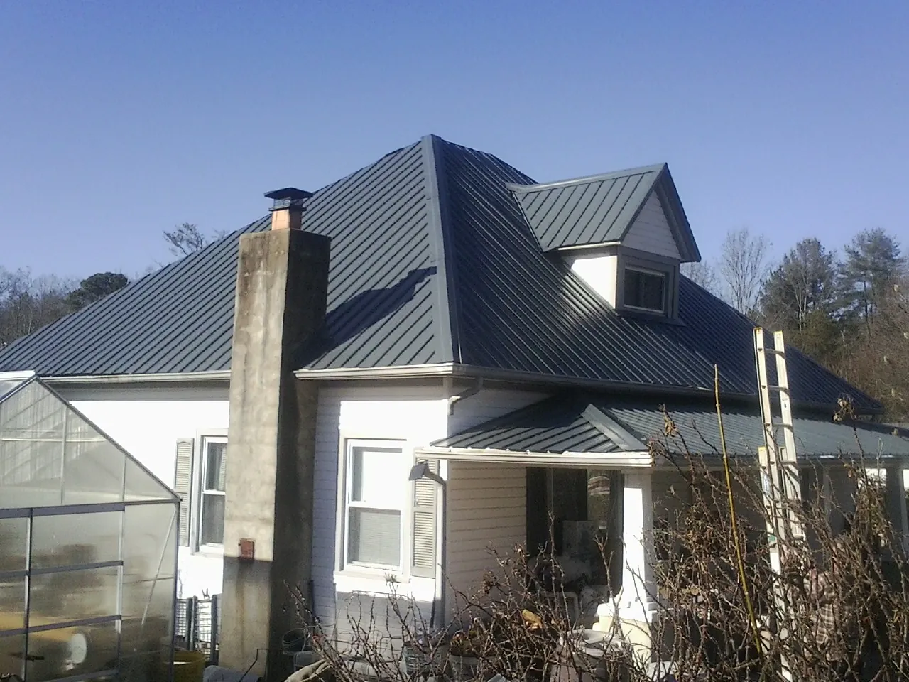 Dark blue standing seam metal roof on a white farmhouse with dormer — Slate & Tile Roof Repair by Roofing Brothers in Callender