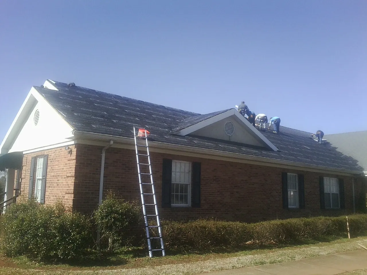 Crew tearing shingles off a brick ranch roof with a ladder set — Metal Roof Repair work by our crew in Callender