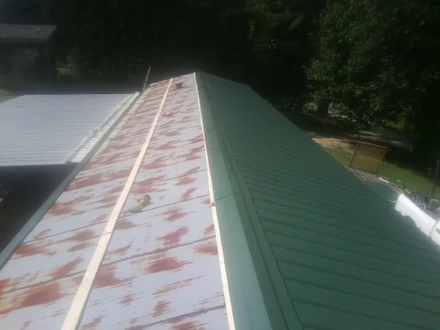 Old rusted panels beside newly installed green metal roofing — Wind Damage Roof Repair by Roofing Brothers in Callender