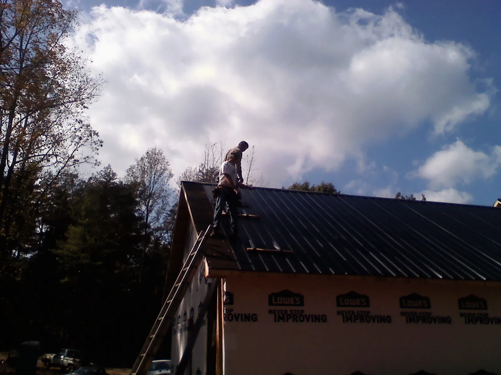 Roofer fastening dark metal panels high against a cloudy sky, from a Roof Inspection job in Callender